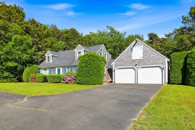 Charming Cape home with 2-car garage, lush lawn, and private wooded setting