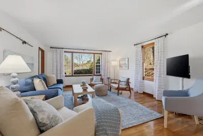 Sunlit living room with big windows, hardwood floors, and cozy seating.