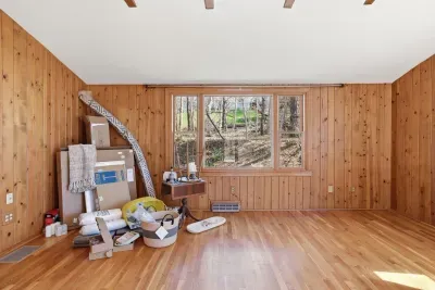 Sunny wood-paneled room with hardwood floors and forest views