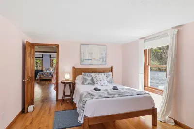 Sunny bedroom with queen bed, hardwood floors, and forest views