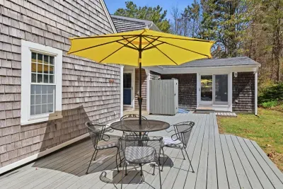 Sunny deck with dining set, umbrella, and outdoor shower—wooded privacy.