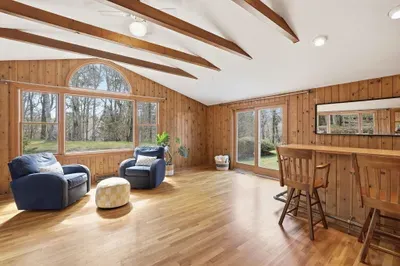 Sunny wood-paneled lounge with beams, bar, and yard access.