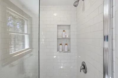 Bright subway-tile shower with niche, glass door, and stocked toiletries