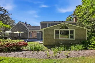 Charming shingle-style home with lush landscaping and outdoor patio