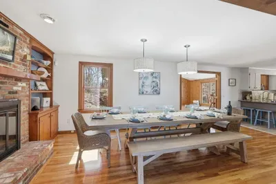 Bright dining room with farmhouse table, fireplace & open kitchen
