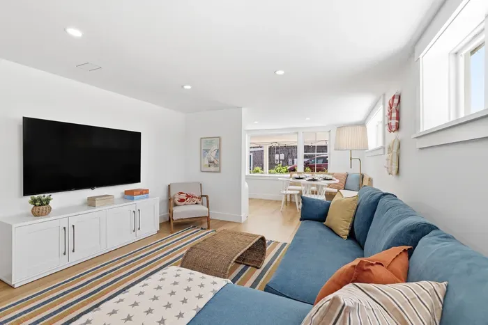 Bright coastal living room with large sectional, TV, and sunny dining nook