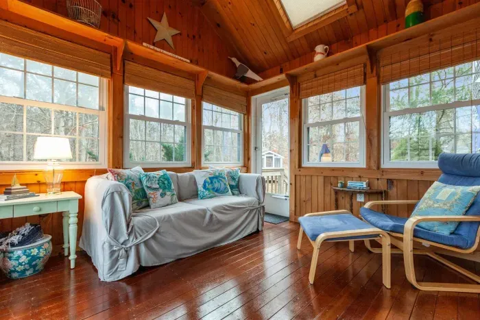 The room is flooded with natural light from multiple large windows that look out onto a wooded area