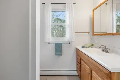 Start your day with natural light! This bright bathroom features a generous window and warm wood vanity