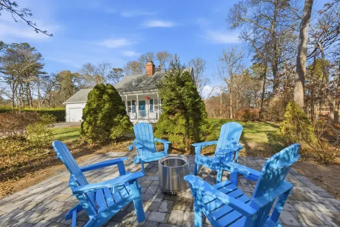 A dedicated stone-paver patio is equipped with bright blue Adirondack chairs centered around a modern fire pit.