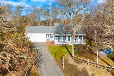 An aerial view showcasing the long, paved driveway leading to the attached garage and the home's scenic, tree-lined perimeter.