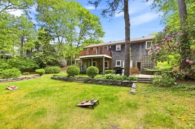 Private backyard with deck, patio, grill, and lawn games under mature trees