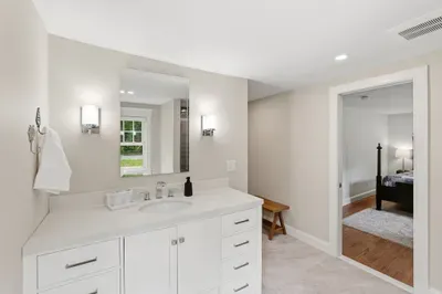 Bright ensuite bath with spacious vanity, modern lighting, and bedroom access
