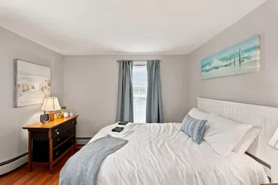 Bright coastal bedroom with cozy linens, natural light, and warm wood floors