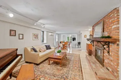 Cozy living room with brick fireplace, piano, and open dining area