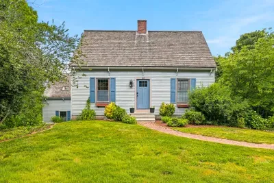 Charming Cape home with lush lawn, brick path, and storybook curb appeal
