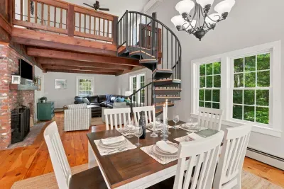Bright loft-style dining and living space with spiral staircase and forest views