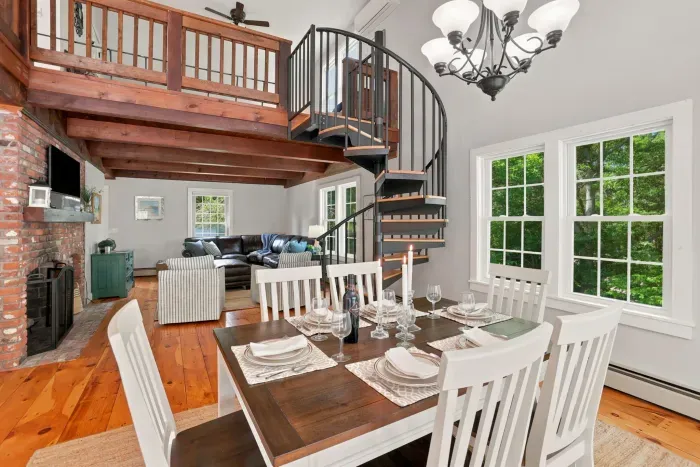 Bright loft-style dining and living space with spiral staircase and forest views