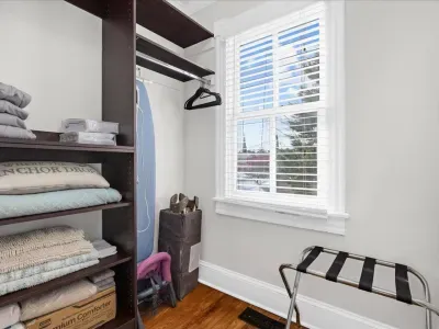 Closet storage area with extra blankets, ironing board, pack and play, and luggage rack.  Located within the Bedroom #2 bathroom.
