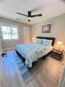 Bright coastal bedroom with king bed, large window, and modern ceiling fan