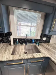 Modern kitchen sink with stone counters, window light, and designer finishes