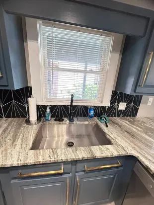 Modern kitchen sink with stone counters, window light, and designer finishes