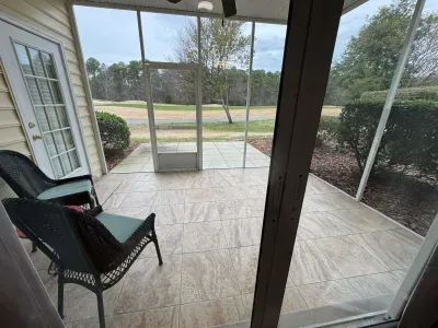Screened tile patio with wicker seating, ceiling fan, and tranquil golf course view