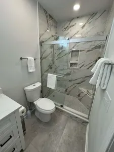 Modern bath with marble tile, glass walk-in shower, and plush towels.