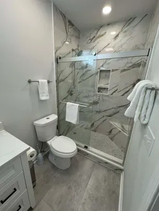 Modern bath with marble tile, glass walk-in shower, and plush towels.