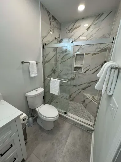 Modern bath with marble tile, glass walk-in shower, and plush towels.