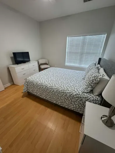 Bright, minimalist bedroom with queen bed, TV, dresser and chair