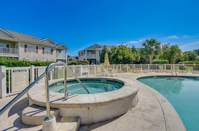 Resort-style pool and hot tub with loungers under sunny skies