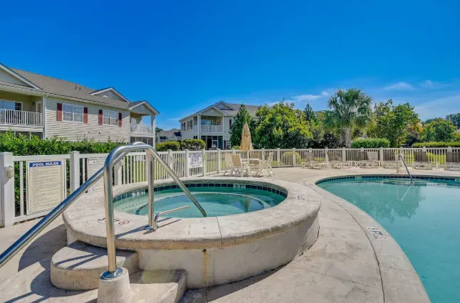 Resort-style pool and hot tub with loungers under sunny skies