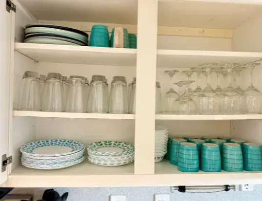 Organized kitchen cabinet with matching dishes, glasses, and bright cups