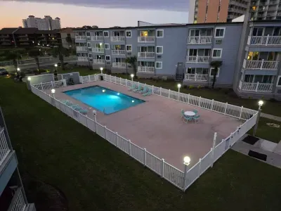 Gated, well-lit pool with loungers and patio seating at condo.