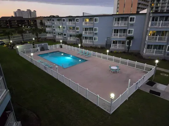 Gated, well-lit pool with loungers and patio seating at condo.