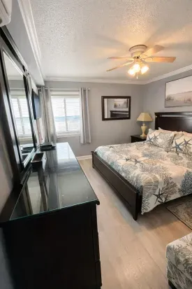 Coastal king bedroom with TV, dresser, ceiling fan, and sunny window