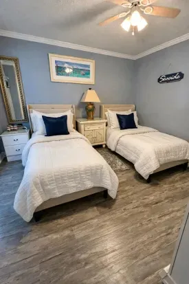 Coastal twin bedroom with crisp linens, ceiling fan, and laminate floors