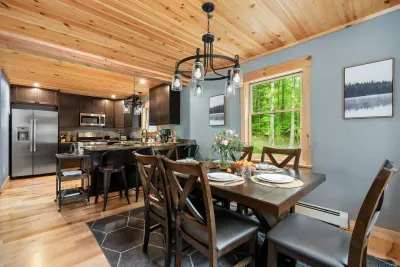 A 6-person dining table seamlessly integrates with a stylish kitchen, featuring a peninsula with seating for four that enhances togetherness. Sleek countertops, modern lighting, and warm wood finishes contribute to the inviting and functional space.