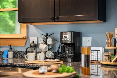 A cozy coffee setup featuring branded mugs, a French Press, coffee maker, assorted teas, honey sticks, and a variety of accessories-perfect for sipping and relaxing. 