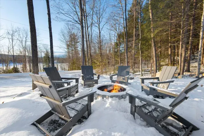 Nestled in Maine's woods, Adirondack chairs encircle a fire pit, perfect for roasting marshmallows and making s'mores. Enjoy the expansive outdoor space, unwind under starry skies, and connect with nature's tranquil beauty in this inviting retreat.