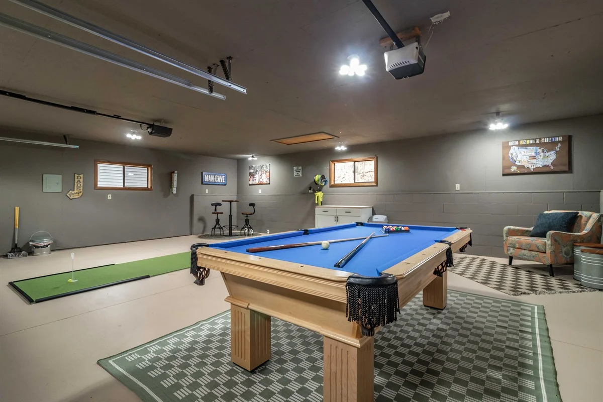 Recreation room with blue billiards table, putting green, and exercise bikes near windows at Brown Bear Cabin, a Clear Trail