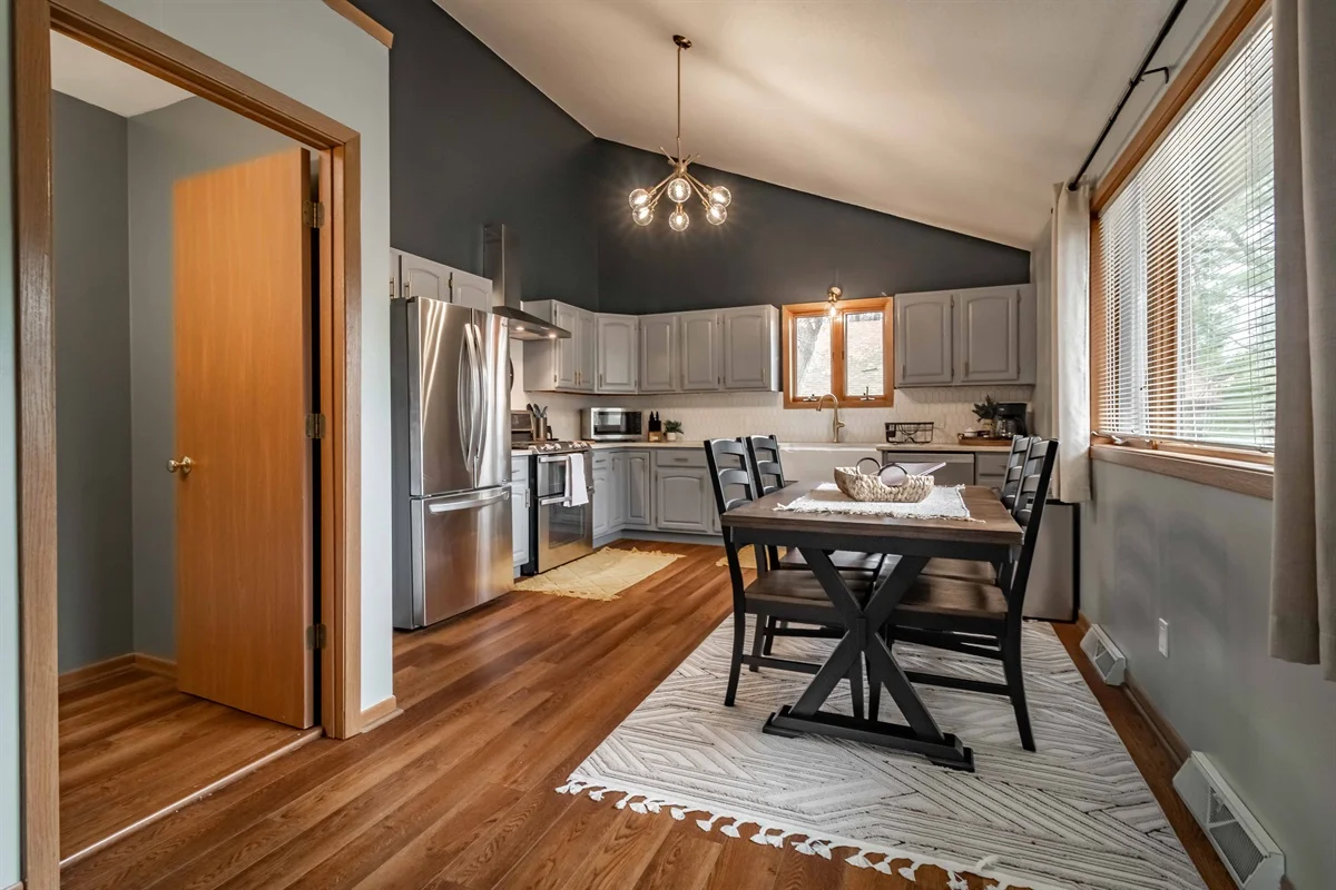 Open-concept kitchen with gray cabinets and stainless appliances beside a dining table, a short-term rental manager
