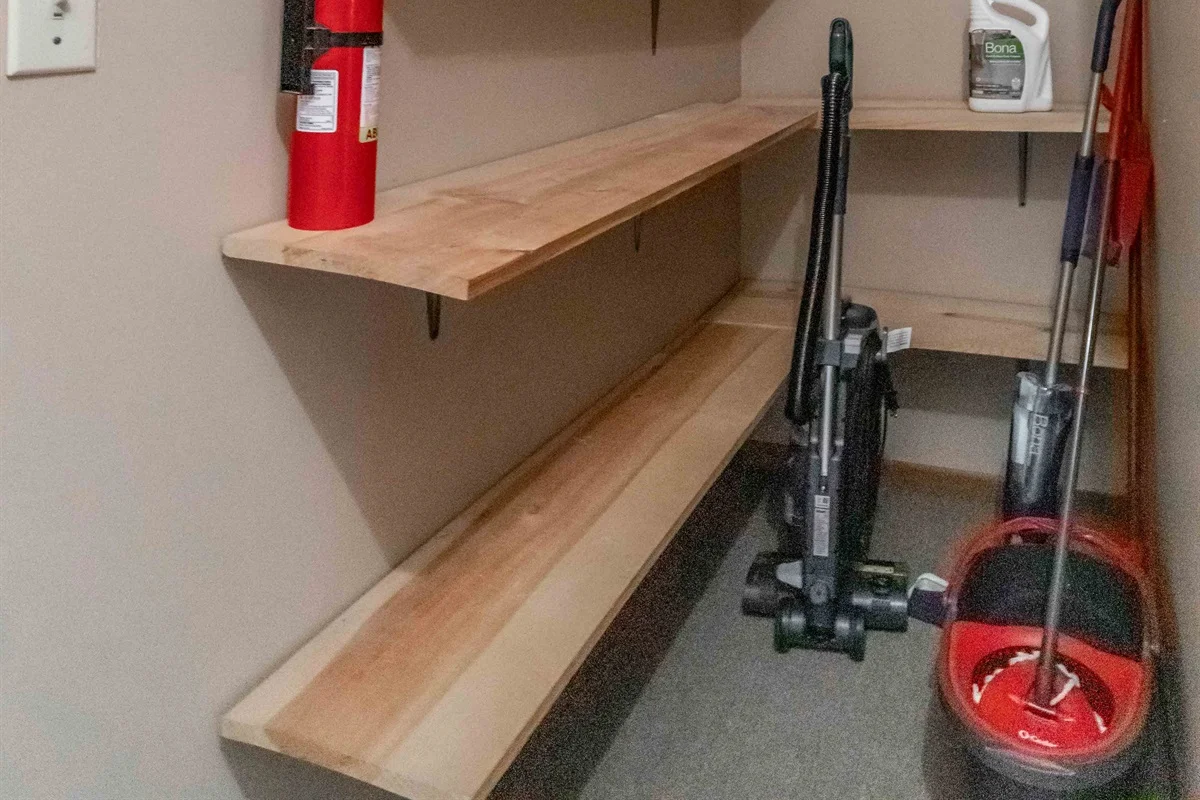 Laundry room with wooden shelving, red fire extinguisher, cleaning supplies and mop on gray floor at a Nekoosa, WI vacation
