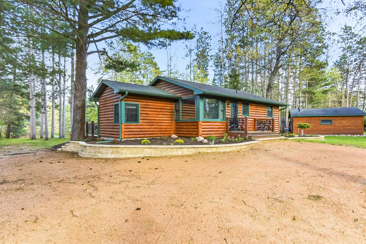 Modern log cabin with orange wood siding, green metal accents, and a front deck among tall pines at Sherwood Shores Cabin in