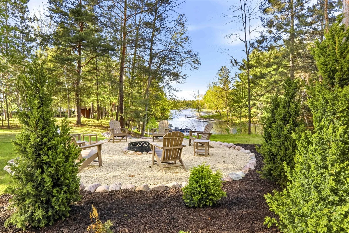 Lakeside fire pit patio with Adirondack chairs and pine trees overlooking waterfront in Minocqua vacation rentals