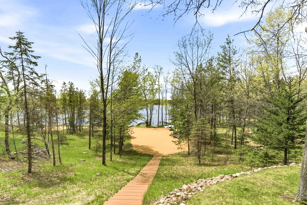 Wooden boardwalk pathway through mature trees toward waterfront lake view at Sunset Getaway in Nekoosa