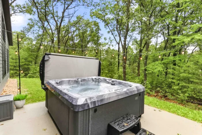 Soak in the hot tub beneath string lights, surrounded by peaceful wooded views for the perfect outdoor escape.