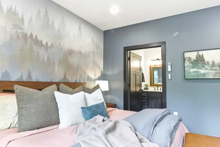 Unwind in a beautifully styled bedroom with soothing woodland accents, plush bedding, and windows that bring the outdoors in.