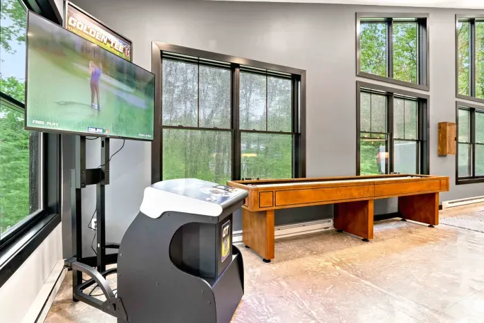 Challenge friends in the game room with Golden Tee arcade golf and shuffleboard, surrounded by bright wooded views.