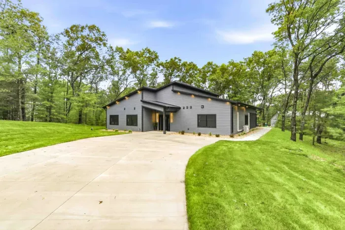 Pull into a modern wooded getaway with a spacious driveway, fresh landscaping, and a peaceful private setting.